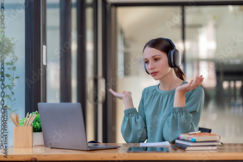 Young woman wearing headphones talking during video call on laptop, remote work and online communication concept.