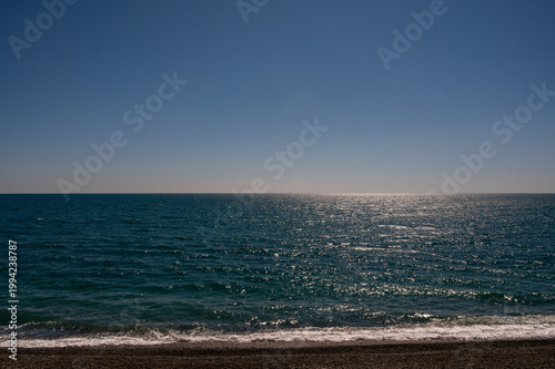 Blue sea horizon with clear sky and pebble beach on sunny day