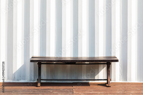 Dark wooden bench against white corrugated metal container wall