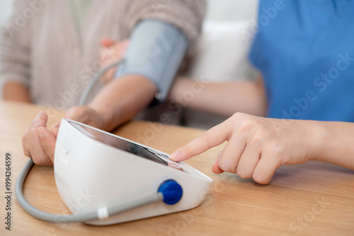 Asian woman nurse measuring blood pressure senior patient, medical checking for hypertension monitoring, caregiver support elderly woman with arterial blood pressure device, routine health checkup.