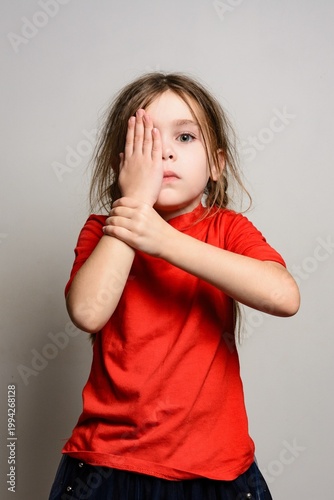 Young girl covering one eye with her hand, playful expression.