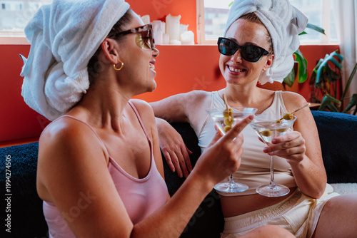 Two women with towels on their heads toasting with martini cocktails