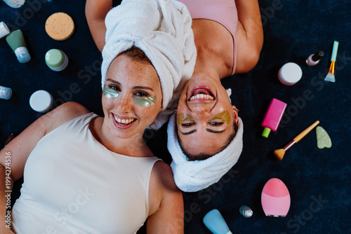 Two happy women lying down, enjoying beauty treatment with under eye patches