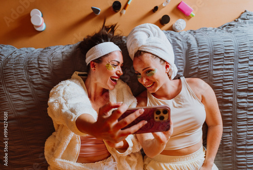 Two cheerful women with golden eye patches taking a selfie after beauty treatment