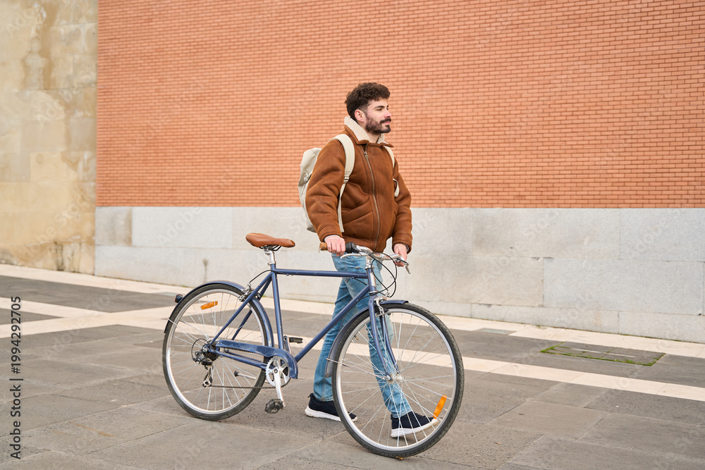 Fototapeta premium Young man walking a bicycle in urban setting