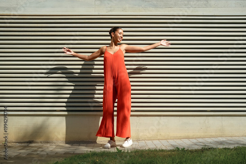 Joyful street pose. Vibrant woman in bright jumpsuit demonstrating joyful movement