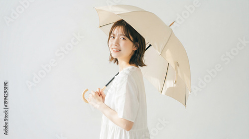 Smiling Japanese woman holding a beige parasol against white background