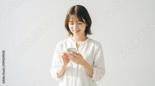 Young Japanese woman operating a smartphone with a gentle smile on white background