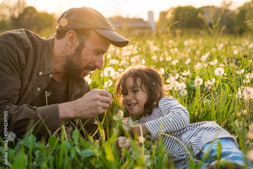 father and daughter playing with dandelions flowers in field at sunset, concept of fatherhood and Parent-child relationships outdoors