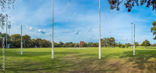 The iconic white AFL goal posts stand tall at Ikon Park (Princes Park) in Carlton, Melbourne, set against a backdrop of lush green turf on a bright, clear afternoon.