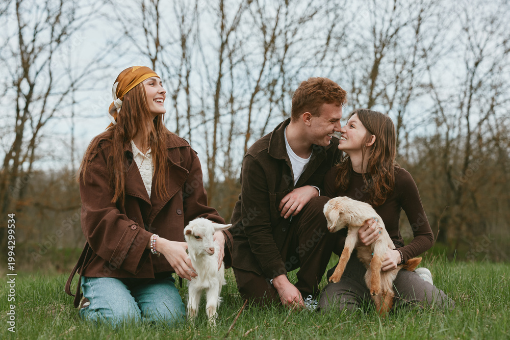 Fototapeta premium Three friends outdoors with dogs enjoying a relaxed moment in a grassy park, warm brown tones, casual outfits, natural light, candid interaction, and a sense of companionship
