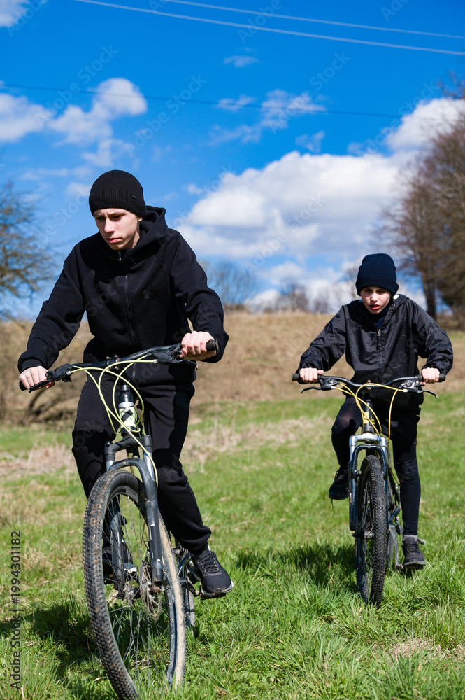 Obraz premium Two young cyclists enjoying a sunny day outdoors, riding their bikes across a grassy field.