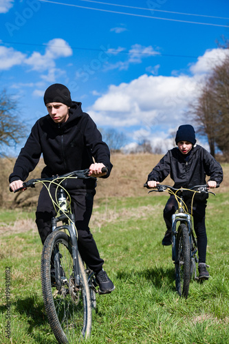 Two young cyclists enjoying a sunny day outdoors, riding their bikes across a grassy field.
