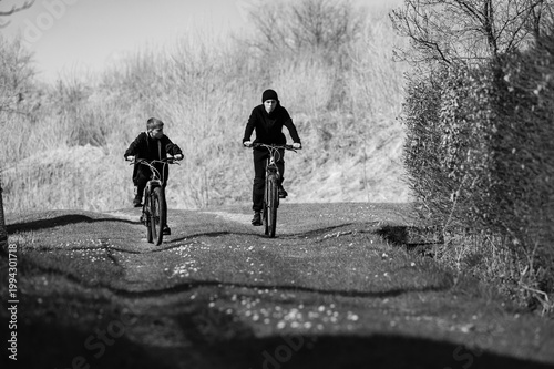 Two boys cycling down a country lane on a sunny day. Enjoyable outdoor activity.