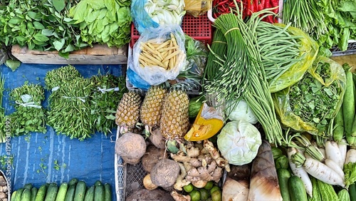 Abundant display of fresh tropical fruits. Vibrant green vegetables. And aromatic root crops for sale at a busy outdoor asian market stall