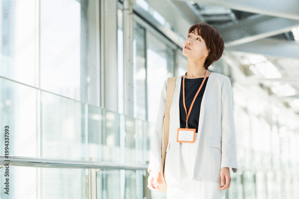 Fototapeta premium ガラスの通路を歩く30代ビジネス女性