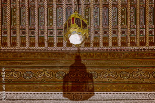 Old gilded lamp hanging from above backed by a lavishly ornate ceiling, room next to the Small Riad garden E side, Bahia Palace. Marrakesh-Morocco-269
