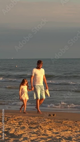 Father and little daughter walk on sand beach at sea at sunset. Summer vacation travel holiday. Vertical shot