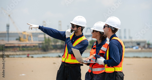 A team of engineers in safety gear walk beside the water at a port