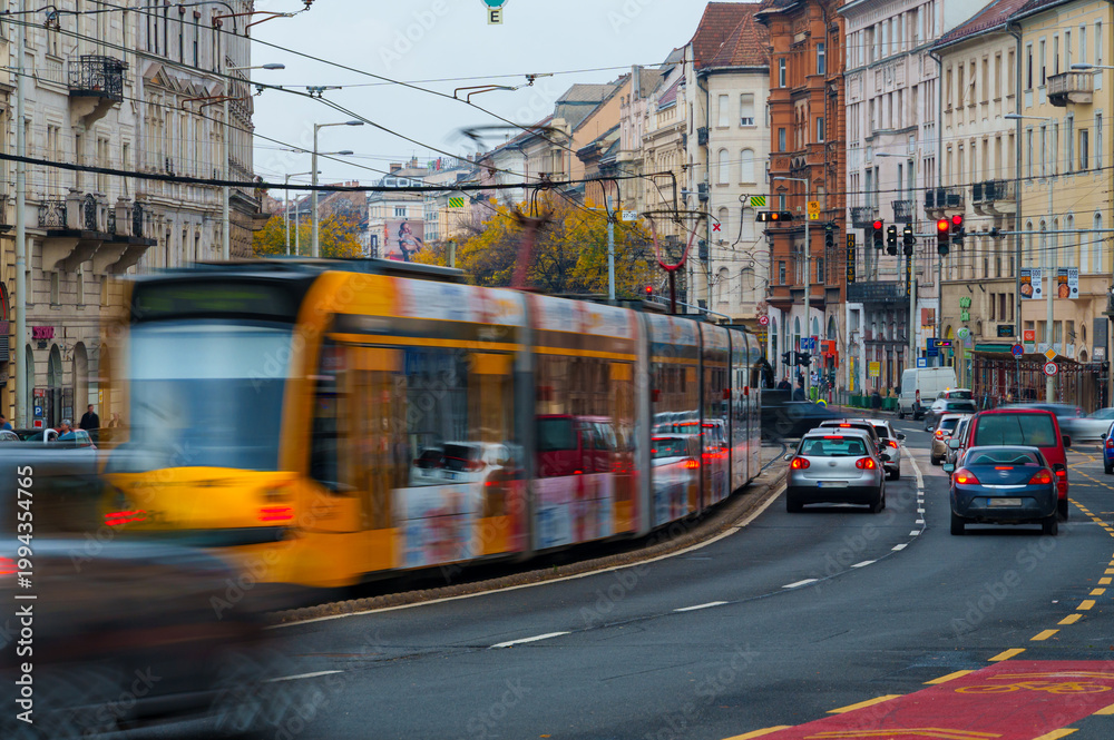 Fototapeta premium Fast moving yellow tram on a wide Budapest street with cars and old buildings