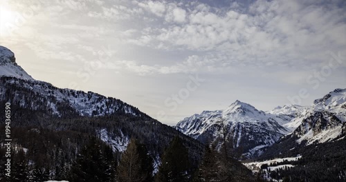 Aerial hyperlapse view of Maloja Pass in the Swiss Alps showing snow-covered peaks, pine forests and a serene winter valley.