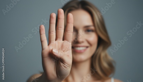 Smiling blonde woman holds up four fingers in close up gesture against a soft blurred studio background