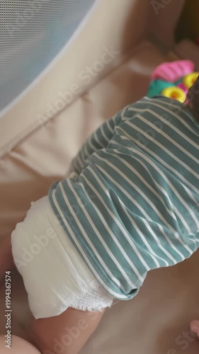 A baby crawls in a play area, reaching for colorful toys. The baby wears a striped shirt and a diaper, exploring the vibrant environment.