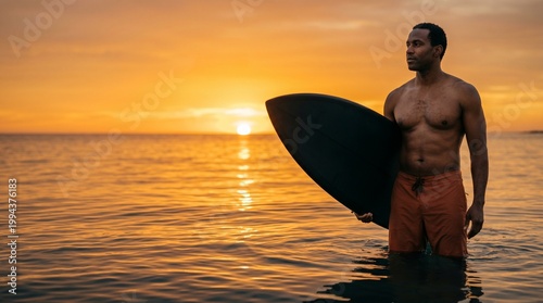 African American man standing in ocean water holding surfboard at golden hour sunset