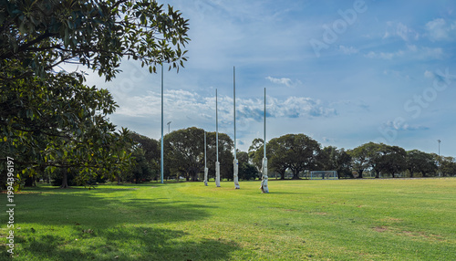 The iconic white AFL goal posts stand tall at Ikon Park (Princes Park) in Carlton, Melbourne, set against a backdrop of lush green turf on a bright, clear afternoon.