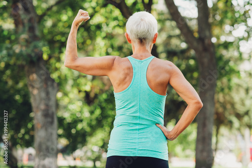 фотографія Senior woman in turquoise athletic tank top flexes arm outdoors in park showing