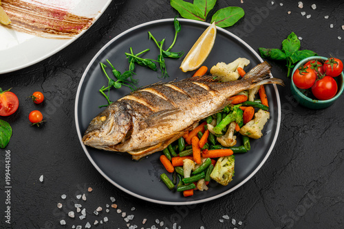 Cuadro en lienzo Whole grilled dorada fish with vegetables on dark background