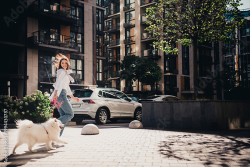 Young woman walking a white dog in an urban apartment complex, smiling and enjoying a sunny day outdoors