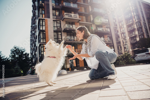 Canvas Print Woman playing with white fluffy dog in urban apartment courtyard on a sunny day