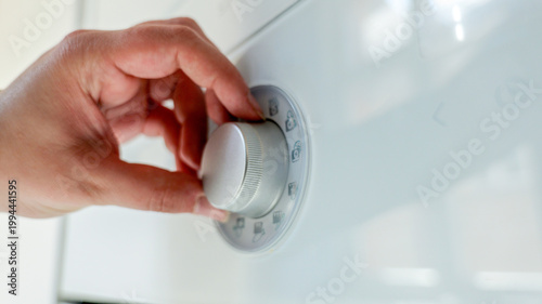 Close-up of a hand turning a dial on a white appliance with various symbols