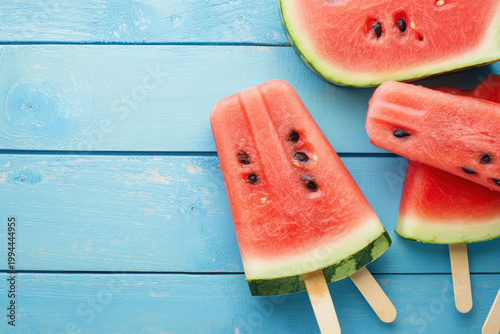 Fresh watermelon popsicles on a blue wooden table with watermelon slices nearby