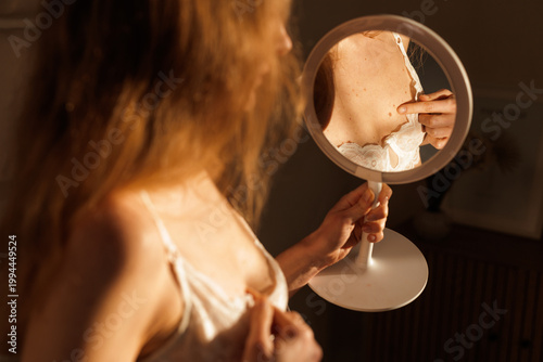 Woman checking moles on chest in mirror for skin cancer prevention and dermatology control