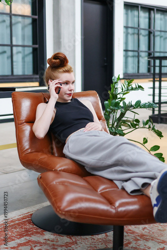 Stylish young woman having a phone call, sitting comfortably on chair.