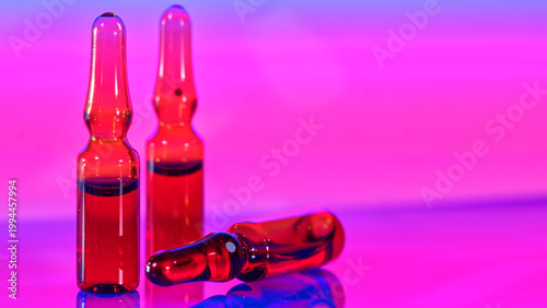 Red glass vials sit on a shiny surface under colorful lighting at a close distance, capturing bright colors and reflections
