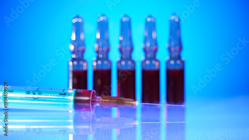 Syringe and vials displayed on a table with blue background during a laboratory setting