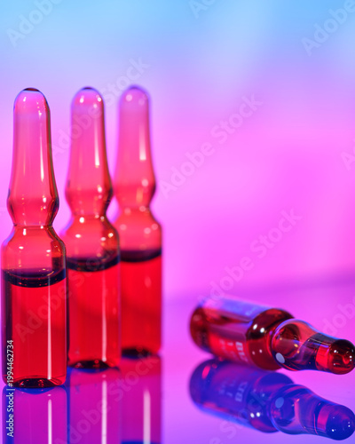 Vials with red liquid are arranged on a table with a colorful background at an indoor setting during the evening