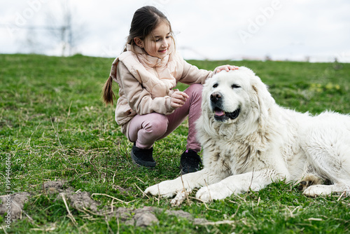 Little girl petting a large white dog on a grassy field showing gentle friendship and outdoor play