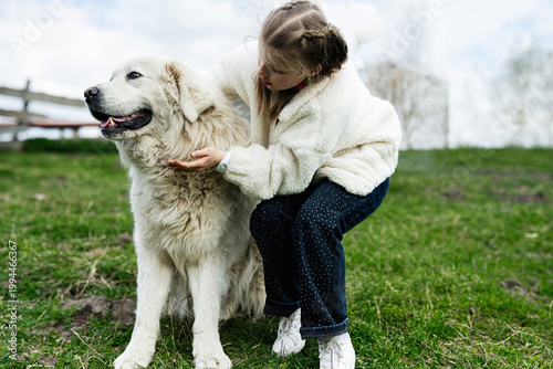 Young girl petting large white dog on grassy field showing gentle friendship and outdoor family moment