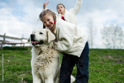 Young girls playing outdoors hugging a large white dog, smiling and enjoying a playful family moment in the countryside