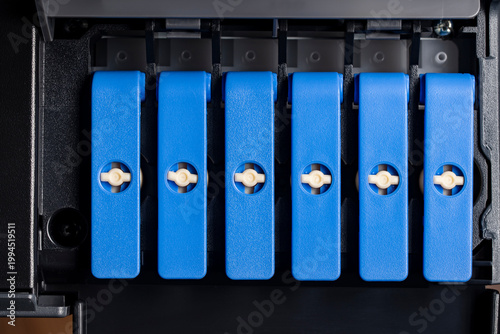 Closeup of blue ink tank caps in photo printer. Macro view of refillable ink tank system caps inside a professional photo printer. Concept of continuous ink supply maintenance and office hardware