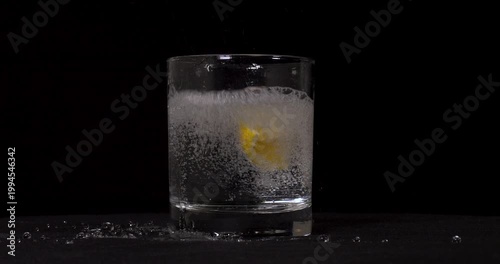 Slow motion shot of soda and lemons pouring into glass on black background.