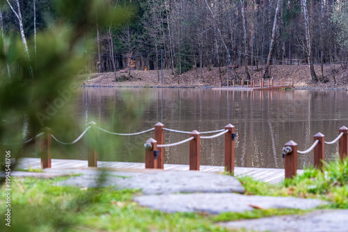  Tranquil scene featuring a serene pond in a park, bordered by lush trees and highlighted by a wooden bridge. The reflective water creates a peaceful ambiance suitable for relaxation.