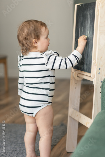 A happy toddler enjoys drawing with chalk on a blackboard, children's scribbles, a home easel for toddlers