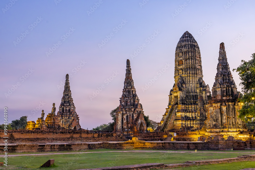 Fototapeta premium Majestic ancient temple ruin under peaceful twilight sky at Wat Phra Si province evoking tranquil awe with illuminated historic architecture and lush green grass field during beautiful evening