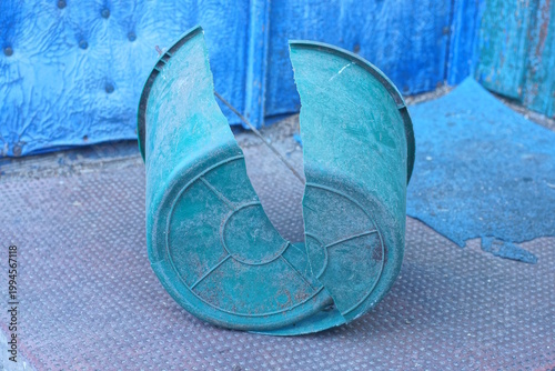 One old broken green plastic bucket stands on the brown floor on the daytime street