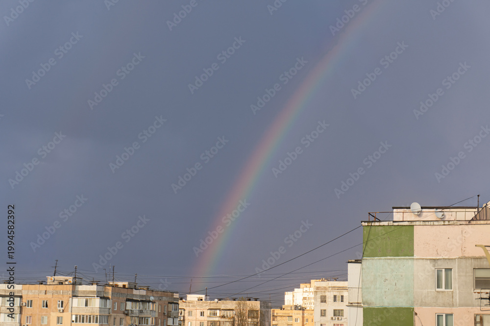 Fototapeta premium Rainbow arch over Soviet-era concrete panel apartment buildings under stormy dramatic sky